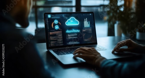 two people collaborating over a laptop showing cloud analytics, code, graphs and dashboards on a dark desk in a dim office with a potted plant by the window, focused and concentrated