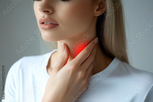 young blonde woman in a white t-shirt holding her throat with her hand, red highlighted area indicating pain, partial face obscured, looking uncomfortable and concerned