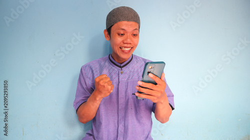 Asian Muslim man holding a cellphone with a happy expression