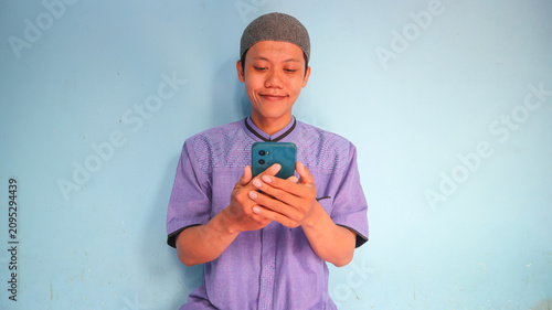 Asian Muslim man holding a cellphone with a happy expression