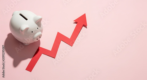 A white piggy bank sits next to a red upward-trending arrow on a pink background, symbolizing financial growth.