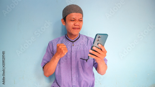 Asian Muslim man holding a cellphone with a happy expression