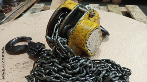 Heavy duty yellow manual chain block hoist with steel hooks on cardboard background
