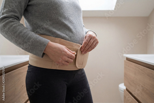 Expectant Mother Wearing Orthopedic Abdominal Brace For Back Support At Home