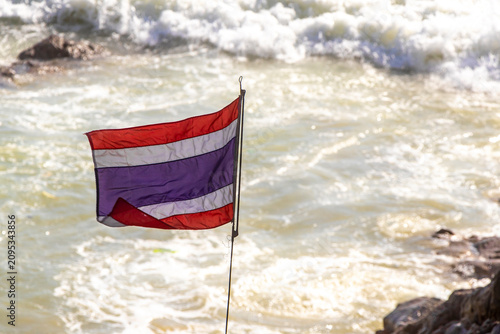 Thai national flag waving in wind above ocean waves Thailand.