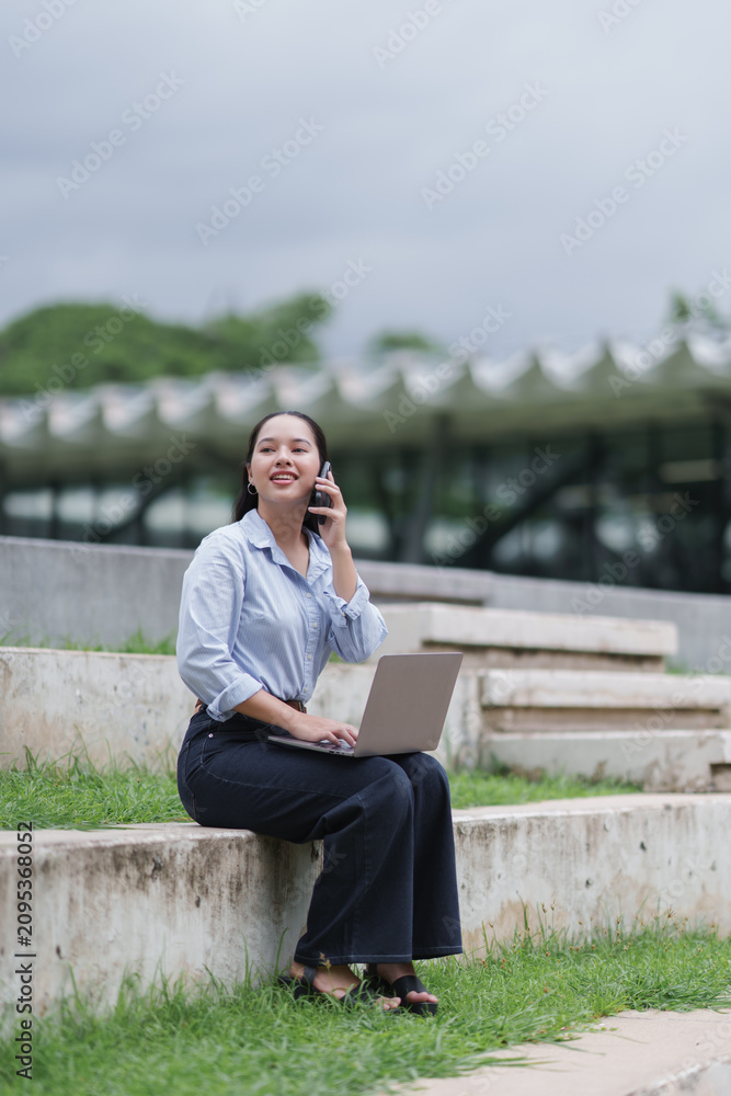 Obraz premium Woman multitasking outdoors, talking on smartphone and using laptop