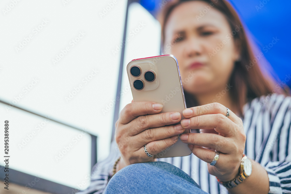 Fototapeta premium Sad and depressed Asian woman looking at smartphone screen facing severe emotional stress and anxiety. Concept of digital burnout, cyber anxiety, technological stress, bad news, mental health crisis,