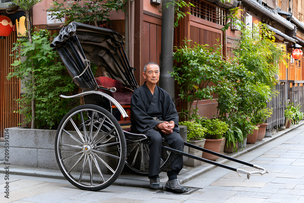 Obraz premium Rickshaw Puller Resting on Stone Street Between Rides in Traditional Attire in Urban Environment