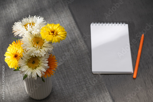 Summer bouquet of double daisies and marigolds with a blank notebook and pencil on a wooden table.