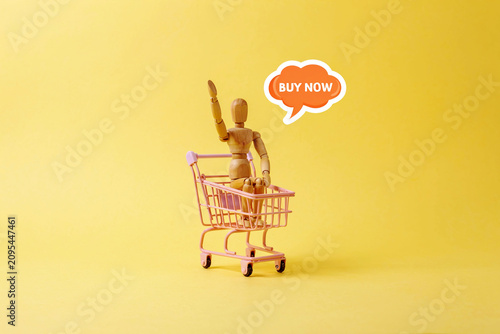 Wooden Mannequin in Shopping Cart with Buy Now Speech Bubble for Online Shopping Concept