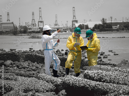 Scientists in chemical protective suits are at a water passage, collecting water samples and analyzing data on laptops to monitor pollution and contamination in the industrial area.