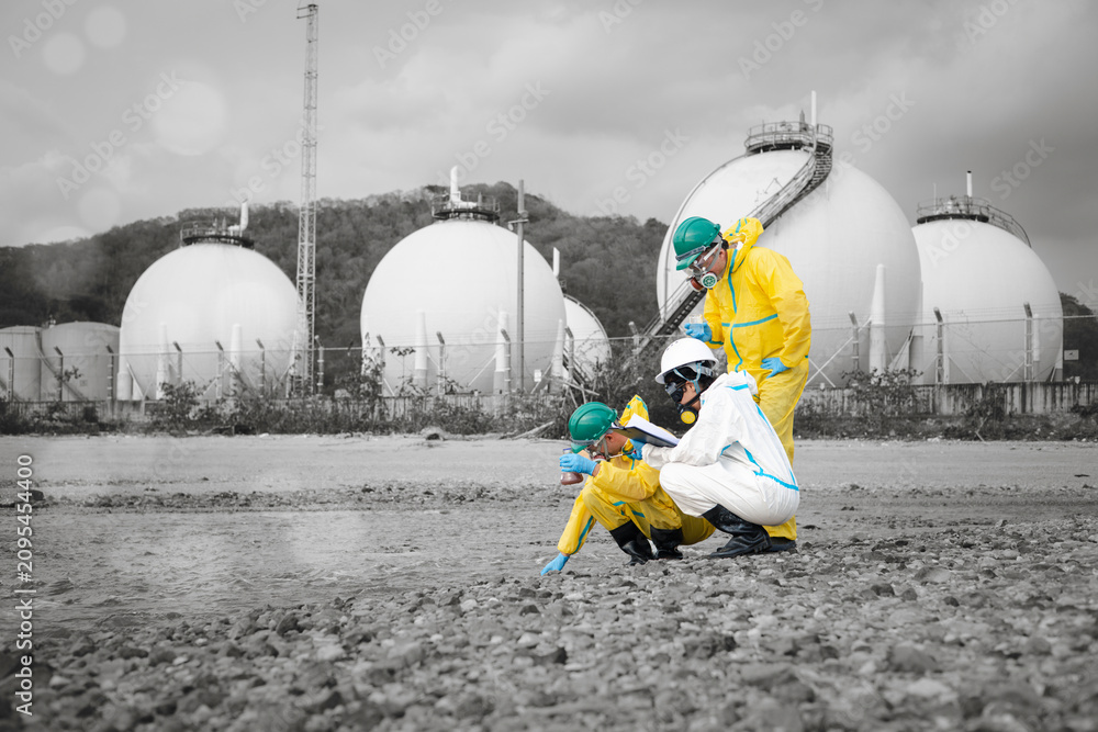 Fototapeta premium Scientists in chemical protective suits are at a water passage, collecting water samples and analyzing data on laptops to monitor pollution and contamination in the industrial area.