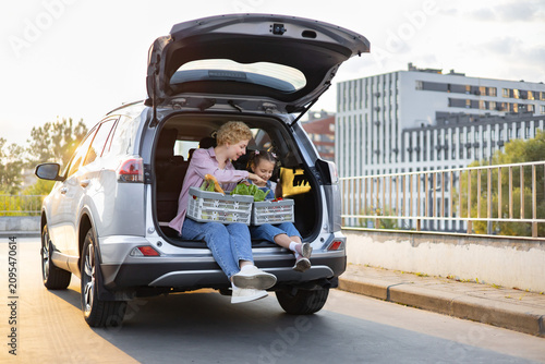 Fotografie A Caucasian mother and her young daughter are sitting in the open trunk of a car