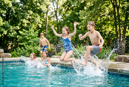Children jumping into backyard swimming pool with splashes and joyful expressions for summer activity banner and family fun background
