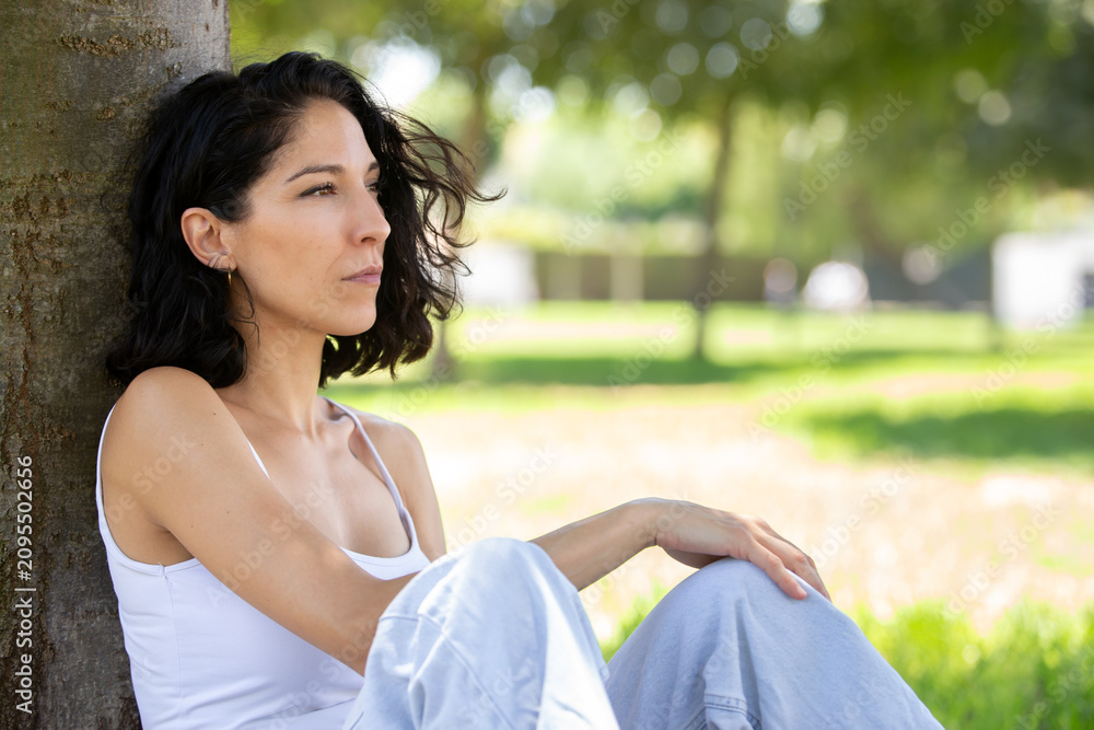 Obraz premium Thoughtful young woman sitting under a tree in a peaceful park