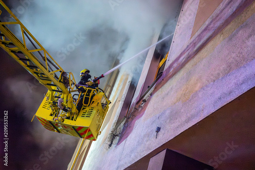 Obraz na płótnie Firefighter battling shopping mall fire from aerial ladder at night