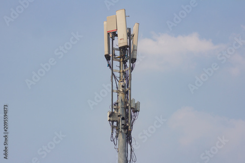 A cellular telecommunication tower pole with various transmitter antennas mounted on top against a bright blue sky background