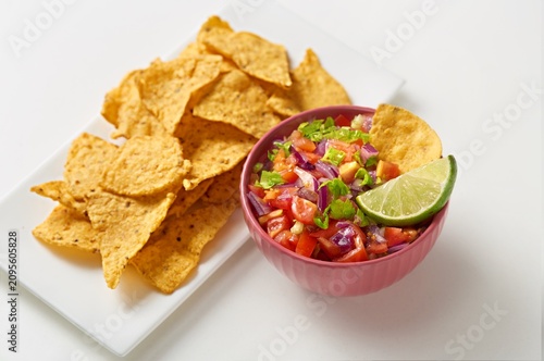 Pico de gallo bowl with a tortilla chips on the side on a white background. Side view