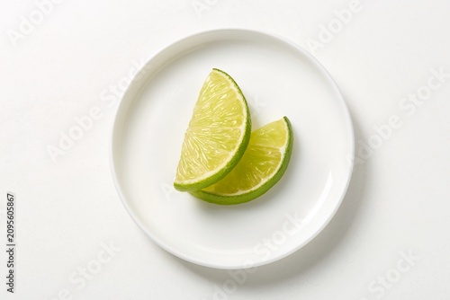 Lime wedges on a white plate, minimalist composition. Top view, negative space