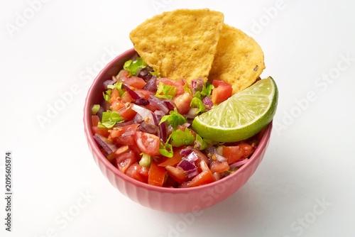 Pico de gallo bowl with a tortilla chips on the side on a white background. Side view