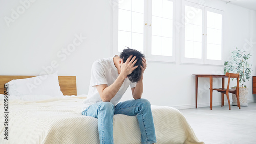 Foto 寝室で悩む男性。疲労、肩こり、つらい、落ち込む、失敗、困る、ストレス、がっかり、不満、ホテル、宿泊