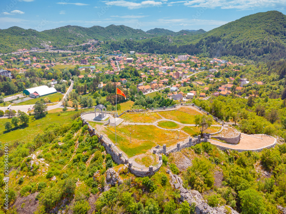 Obraz premium Montenegro flag flying high on Orlov Krs, overlooking historical capital Cetinje town and surrounding green mountains