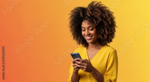 Happy young woman with curly hair looking at her smartphone against yellow background