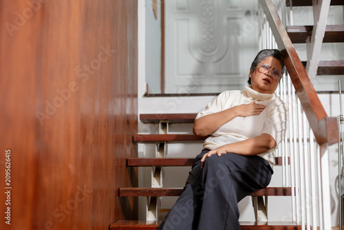 Konstfotografi Senior elderly woman sitting on wooden staircase at home expressing severe chest