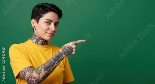 Young person with tattoos pointing to the side against a green background