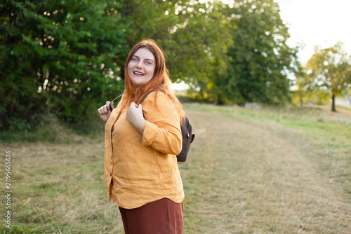 Smiling Red Haired Woman Backpacker with Backpack Hiking in Green Forest