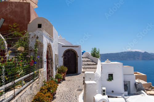 Fotografie Narrow cobblestone street with white Cycladic houses and dark wooden doors in Oia, Santorini