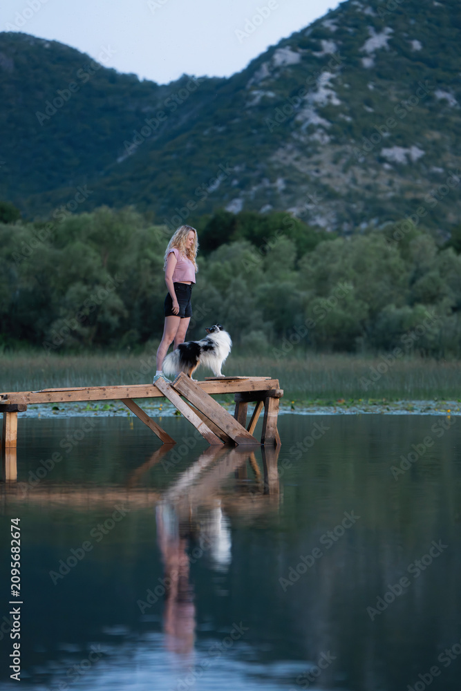Fototapeta premium Woman Enjoying Peaceful Evening on Wooden Pier over Calm Lake with Mountain Reflections