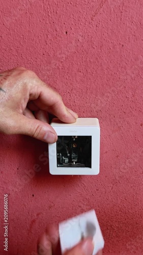 Electrician hands installing white electrical outlet on red wall
