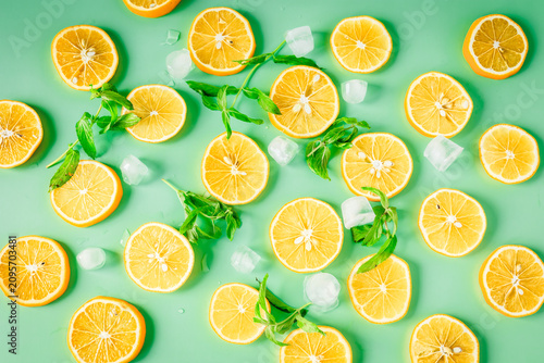 Foto Lemon slices with mint leaves, ice cubes and water drops on a green background,