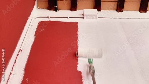 Painter applying white paint over red wall
