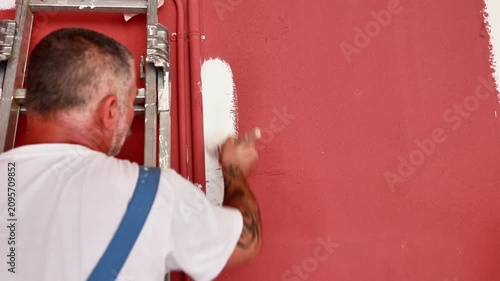 Professional painter applying white paint on a red wall