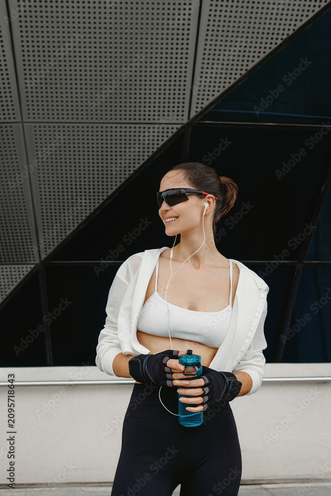 Obraz premium Smiling fit woman holding water bottle by building facade