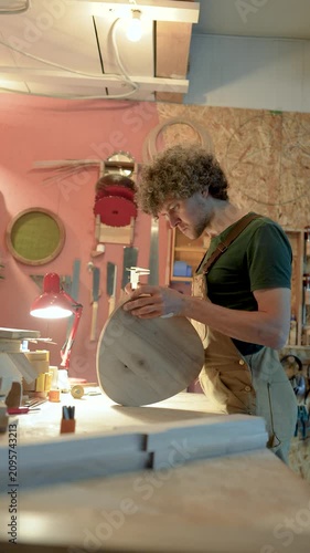 Carpenter manufacturing wooden furniture in workshop, using calipers to check precise fitting of chair details, wood workshop working progress, focused man examines stool parts before assembling.