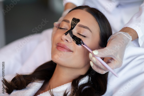 Foto Happy lady enjoying charcoal facial treatment with purifying mask applied across