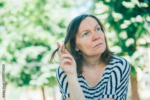 Pensive woman thinking outdoors portrait sitting in park on sunny day reflective mood,