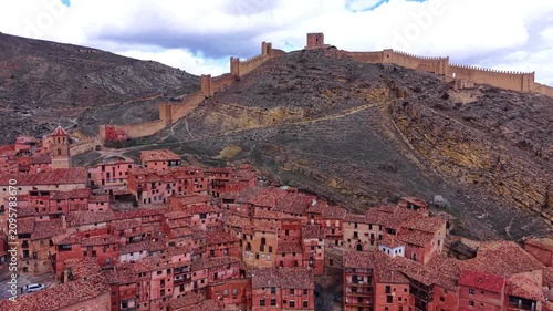 Well-preserved medieval fortress walls crown a rocky ridge above Albarracin's pink-hued terracotta rooftop village with church tower, Teruel, Aragon, Spain
