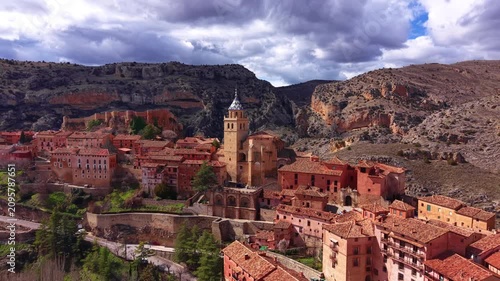 Panoramic view of Albarracin, Teruel, Spain, showcasing the cathedral bell tower, terracotta rooftops, castle walls, and dramatic storm clouds over rocky Aragon landscape