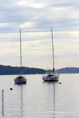 A calm coastal waterscape with two moored sailboats floating on still water.