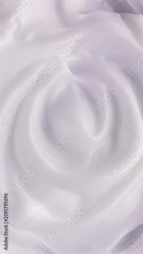 White Cream Swirling. Thick glossy cream moves in smooth folds, creating a soft abstract cosmetic texture.