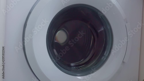 Washing machine drum slowing down spin with water and clothing swirling in circular door window
