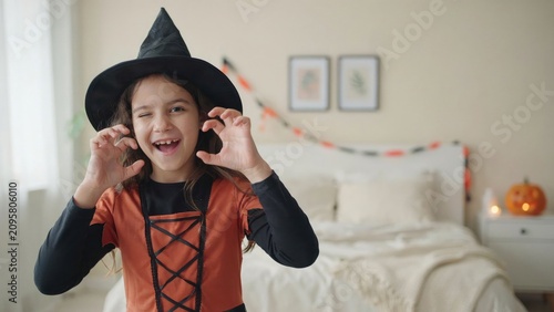 Young girl in witch costume playfully posing for halloween bedroom setting