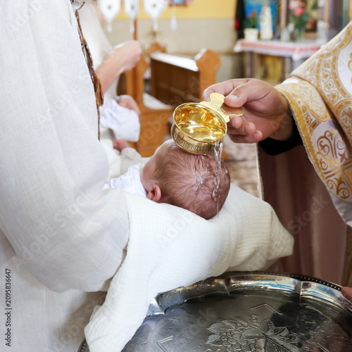 фотографія Priest pours holy water over a baby's head during an Orthodox baptism ceremony inside a church