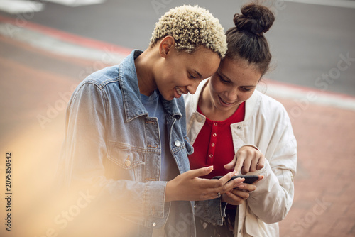 Two young women checking smartphone in the city