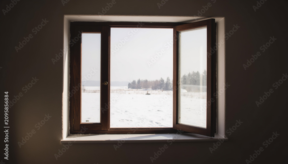 Fototapeta premium Open rustic wooden window frame looking out to beautiful winter snow covered landscape view from dark indoor room