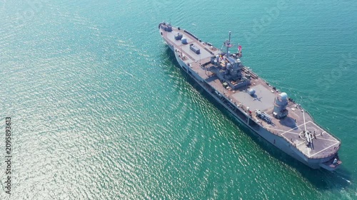 Amphibious Assault Ship. Navy aircraft carrier smoothly navigates turquoise waters beneath hazy sky. This powerful image evokes maritime strength and strategic operation within dynamic coastal environ